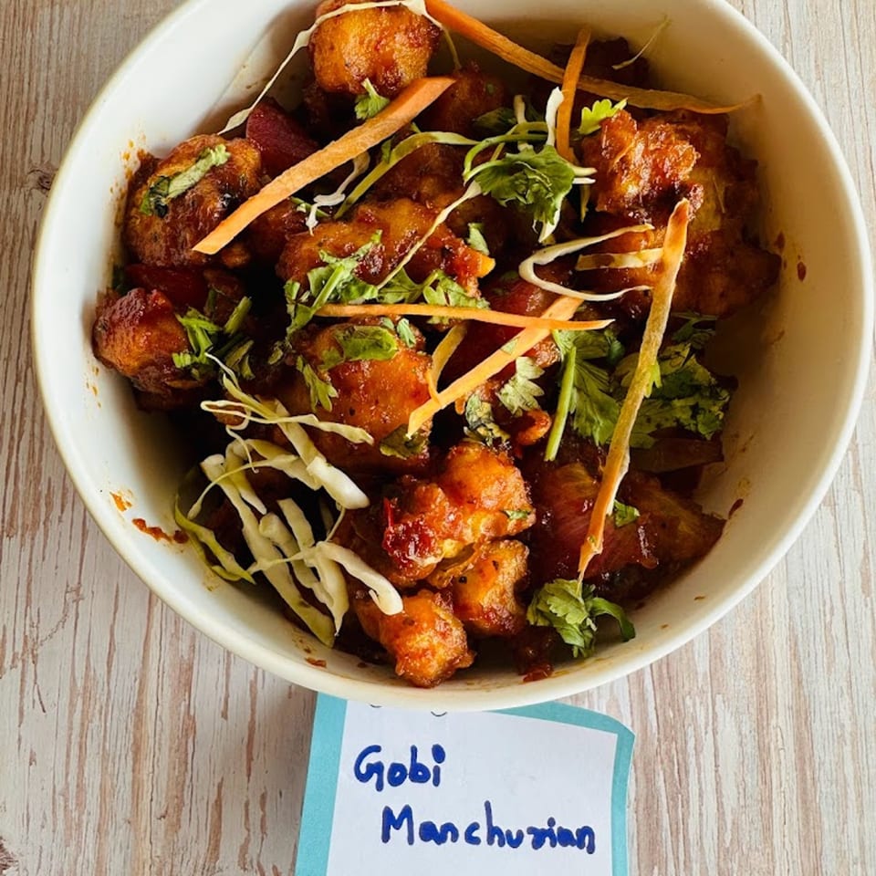 A bowl of Avinya Indian Cuisine's Gobi Manchurian, garnished with shredded carrots, cabbage, and cilantro.